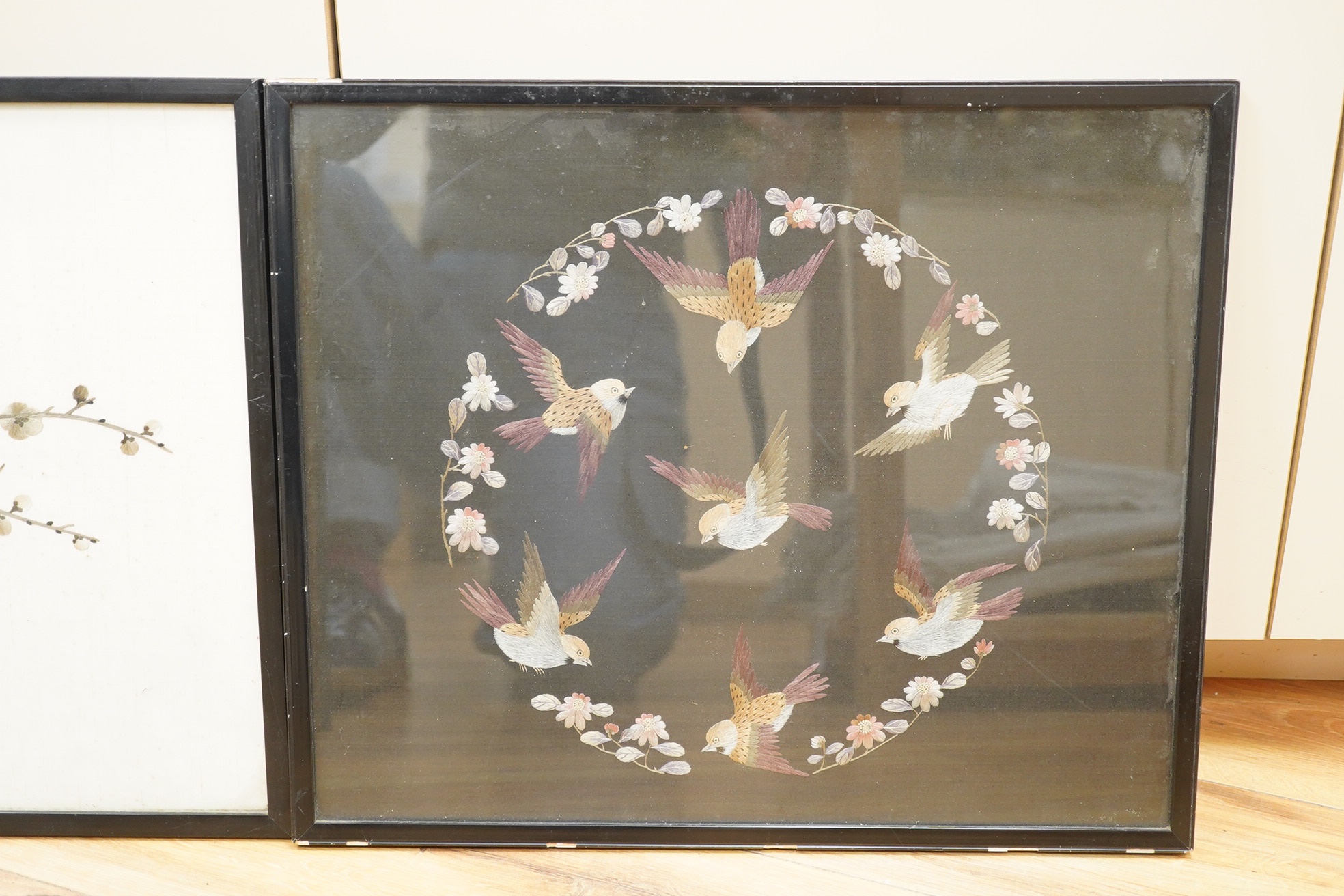 Two Chinese polychromed silk embroidered panels, early 20th century, one on a black silk ground of birds and flowers, the other on a red background of flowers and a monochrome silk embroidered panel of birds and flowers,